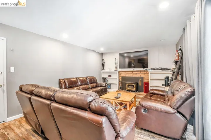 Living area featuring wood-finish flooring, a brick fireplace surround with a wood stove, recessed lighting, and built-in shelving