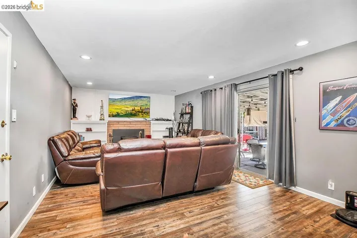 Living area featuring wood-finish flooring, a brick fireplace, built-in shelving, recessed lighting, and sliding glass doors opening to the exterior