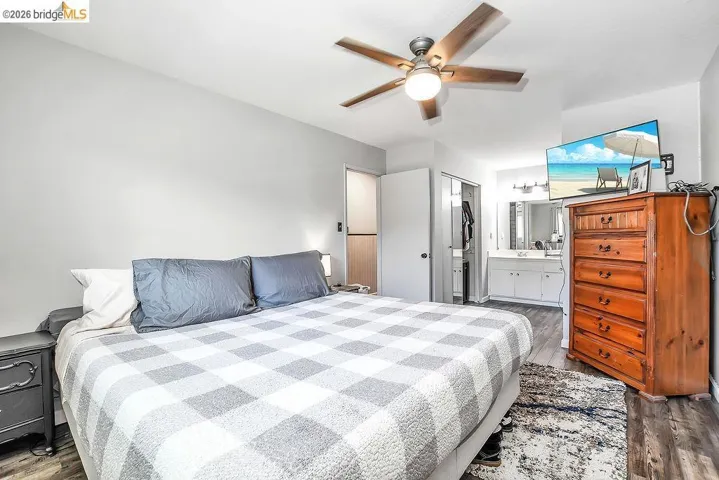 Bedroom featuring wood-finish flooring, a ceiling fan with integrated lighting, and direct access to a vanity area with dual sinks