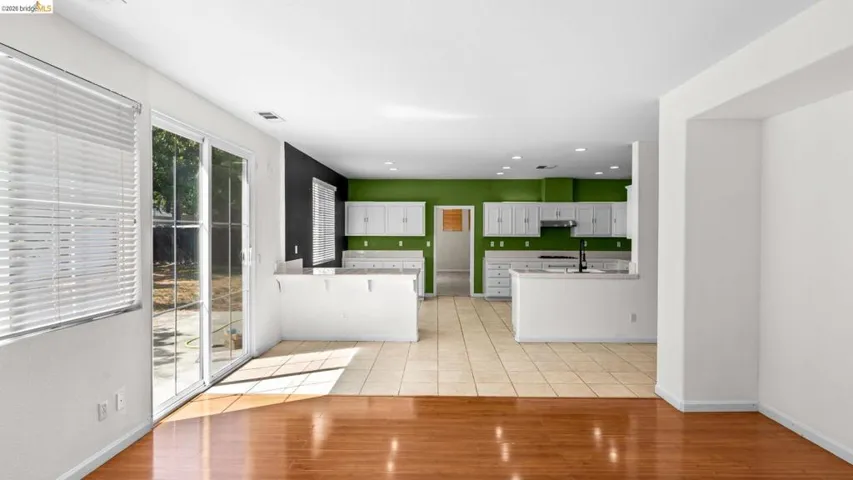 Open-concept living area featuring wood-finish flooring, sliding glass doors to the exterior, and an open kitchen with white cabinetry, light countertops, and tile flooring