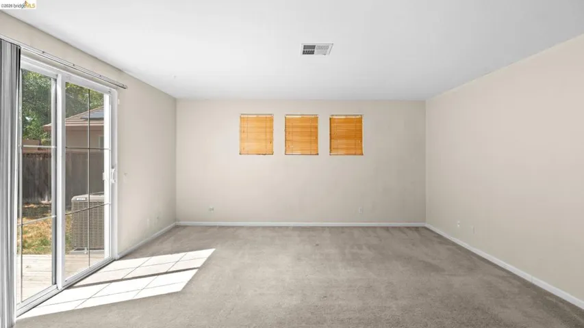 Spacious room featuring light-colored walls and grey carpet flooring