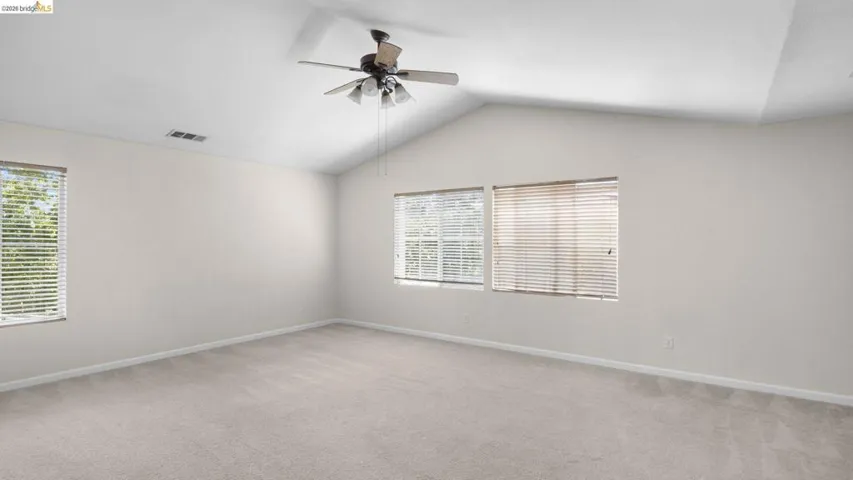 Spacious room featuring vaulted ceilings, light-colored carpeting, multiple windows with blinds, and a ceiling fan with integrated lighting
