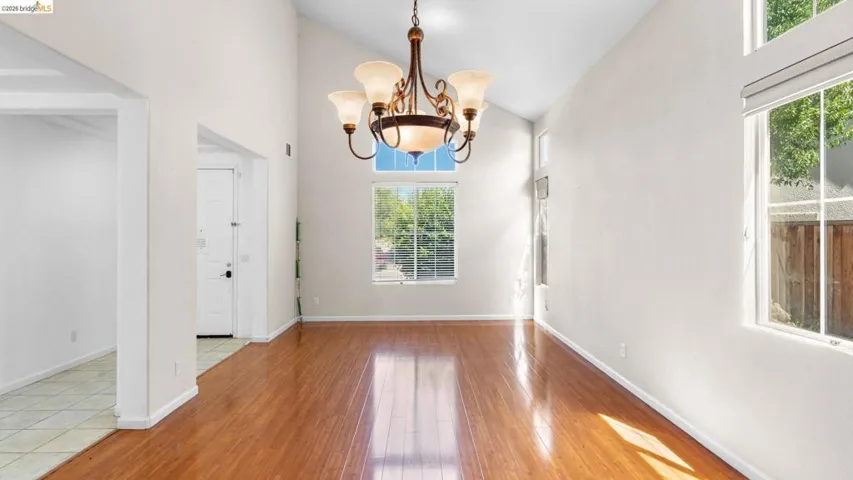 Vaulted ceilings featuring a decorative chandelier, wood-finish flooring, and multiple windows