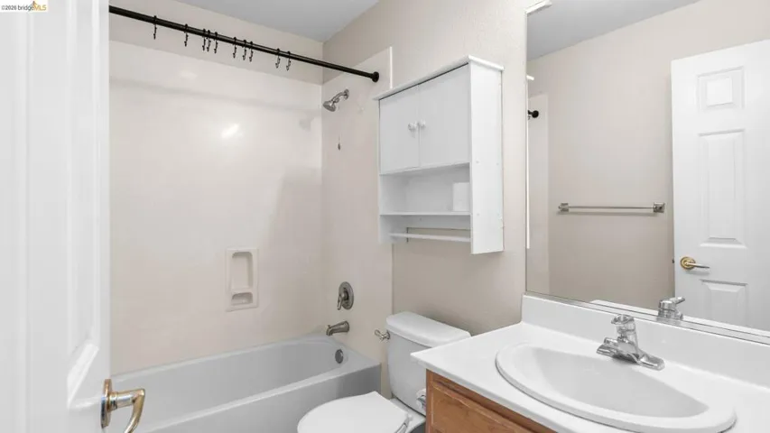 Bathroom featuring a white bathtub with an integrated shower, a white vanity with a single sink, a wall-mounted medicine cabinet, and a white toilet
