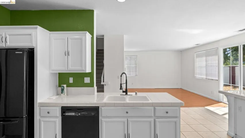 Kitchen featuring white cabinetry, tile countertops, a double basin sink with a black pull-down faucet, and a black dishwasher
