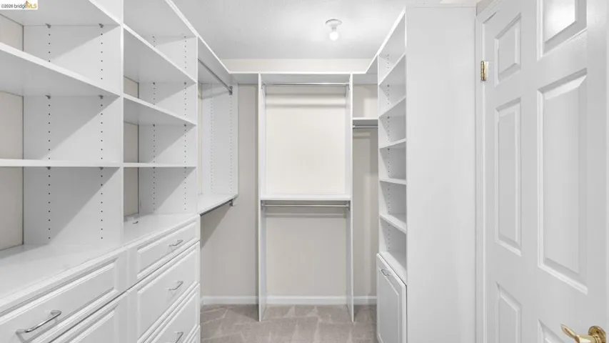 Custom closet system featuring white cabinetry, multiple shelving units, pull-out drawers with chrome hardware, and hanging rods