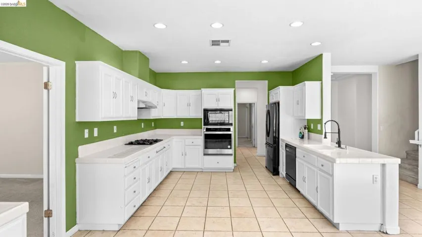 Spacious kitchen featuring white cabinetry, light-toned tile flooring, and integrated stainless steel appliances