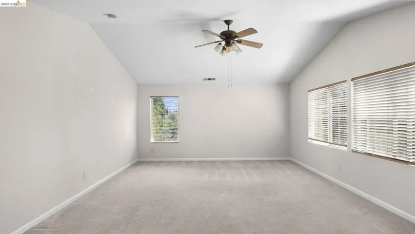 Vaulted ceiling room featuring light beige carpeting, multiple windows with blinds, and a ceiling fan with integrated lighting
