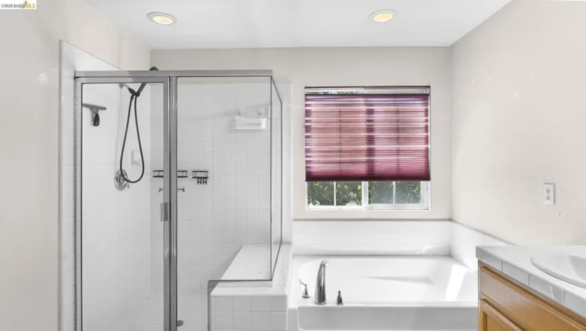 Walk-in shower with clear glass enclosure and integrated bench seating, accompanied by a built-in soaking tub with deck-mounted fixtures