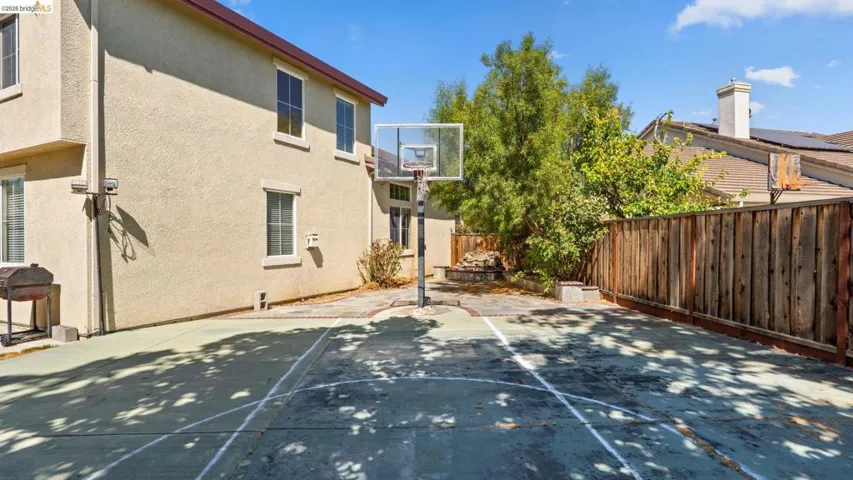 Spacious backyard featuring a dedicated sport court with a basketball hoop, surrounded by a wood fence and mature trees