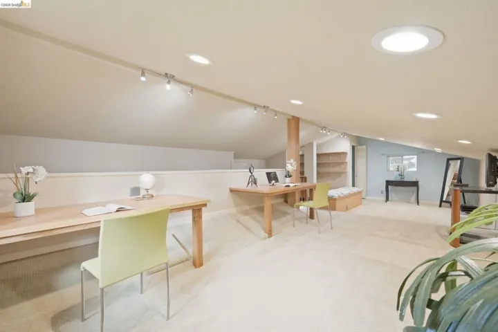 Spacious loft area featuring sloped ceilings, recessed lighting, track lighting, and built-in shelving
