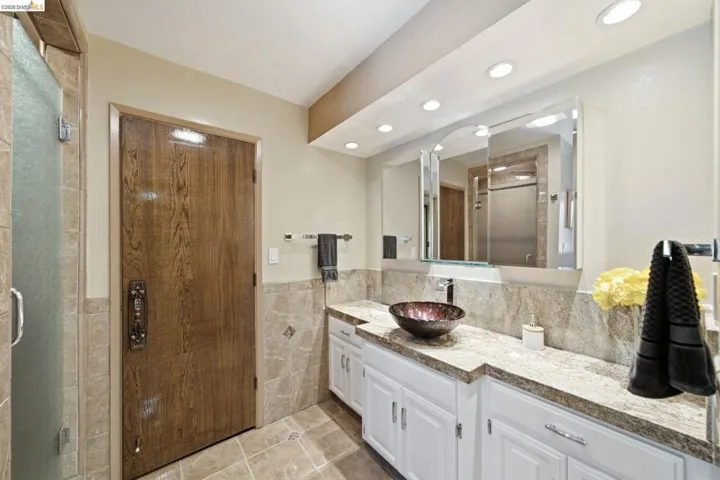 Bathroom featuring a vessel sink, stone countertop, white cabinetry, and recessed lighting