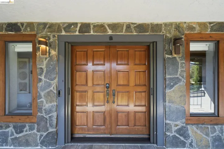 Double wooden panel doors framed by stone veneer siding and wood-framed windows