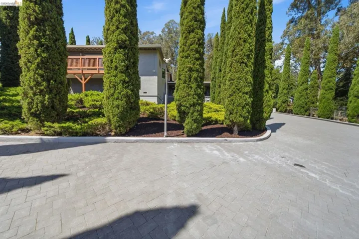 Herringbone pattern paver driveway with lush landscaping and mature columnar evergreen trees
