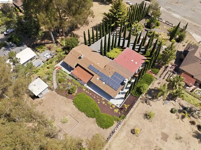 Terracotta tile roof with solar panel array, mature landscaping, tiered garden beds, and an additional detached structure