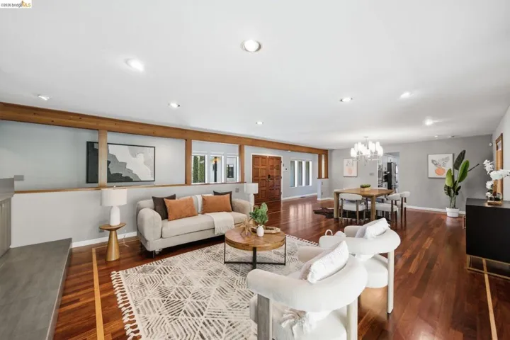 Spacious living area featuring rich wood-finish flooring, a wood beam architectural detail, recessed lighting, and a prominent dining area with a chandelier