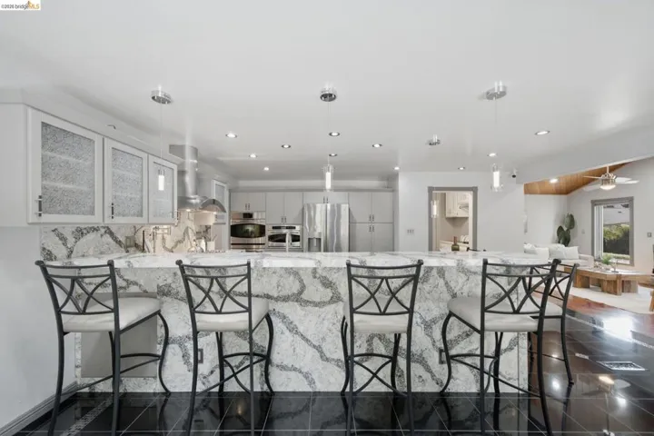 Kitchen featuring a large waterfall island with integrated seating, recessed lighting, pendant lighting, stainless steel appliances, and black tile flooring