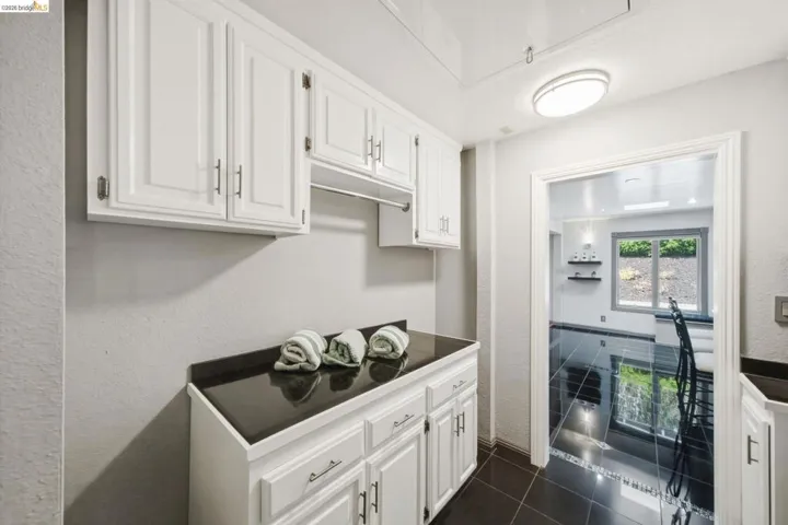 White cabinetry with brushed nickel hardware, black countertop, and black tile flooring