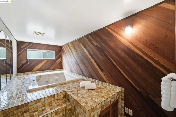 Recessed jetted tub surrounded by mosaic tile steps and platform