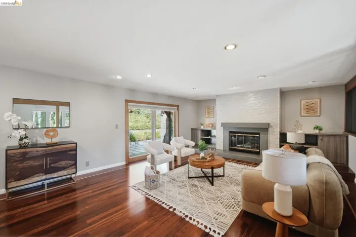 Living area featuring rich wood-finish flooring, a contemporary fireplace with a textured tile surround and stone mantel, recessed lighting, and sliding glass doors opening to the exterior