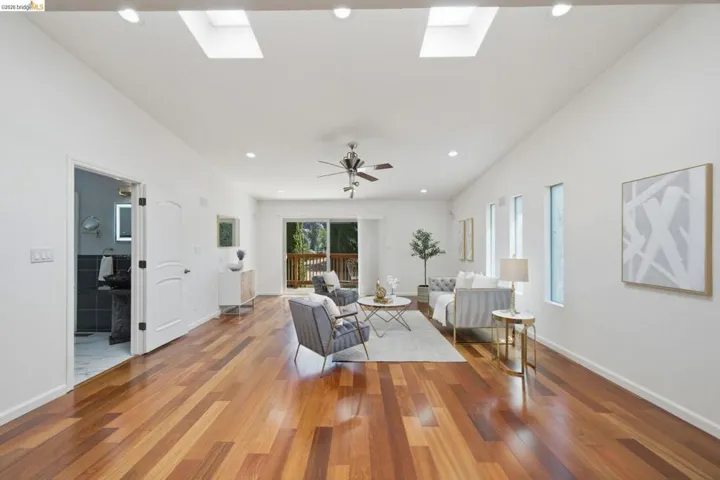 Spacious living area featuring rich wood-finish flooring, recessed lighting, and dual skylights