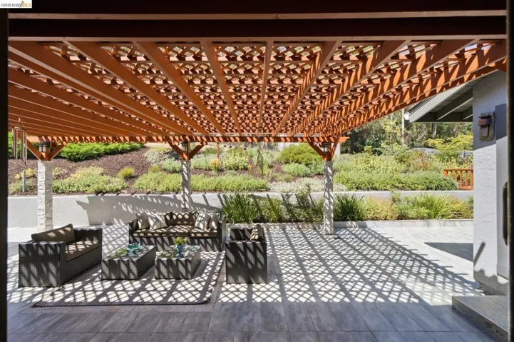 Expansive patio featuring a decorative wooden pergola, tiled flooring, and multiple support columns with stone detailing