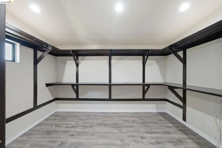 Room featuring extensive built-in dark wood shelving and desk space, recessed ceiling lighting, light gray wood-finish flooring, white baseboards, and a small casement window