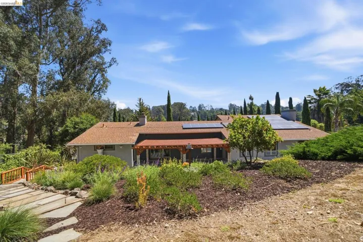 Ranch-style residence featuring a brown shingle roof, solar panels, and a covered porch with a wood-stained pergola