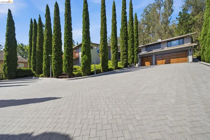 Paver stone driveway leading to a residence featuring a modern exterior, wood-finish garage doors, and an upper-level window bank