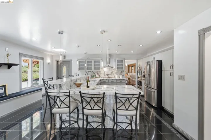 Kitchen featuring a large central island with waterfall-edge countertop, black tile flooring, light gray cabinetry, and stainless steel appliances