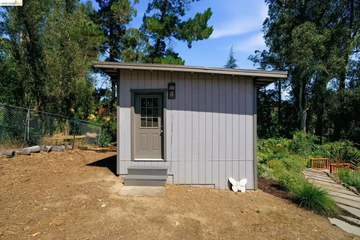 Freestanding structure featuring board and batten siding, a single entry door with window panes, and a small exterior light fixture