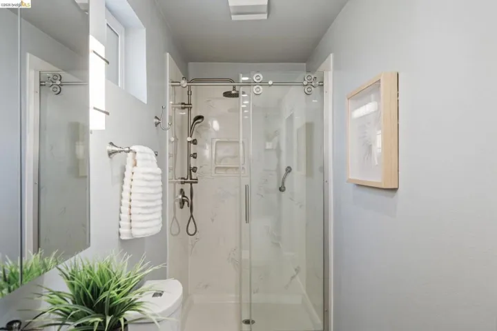 Walk-in shower with sliding glass door, multi-function shower system, integrated shelving, and support bar