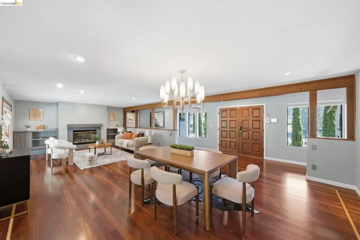Expansive living area featuring rich wood-finish flooring, a contemporary fireplace with a stone mantel, recessed lighting, and exposed wood beams