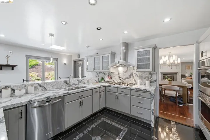 Contemporary kitchen with light grey cabinetry, granite countertops, and a full-height granite backsplash