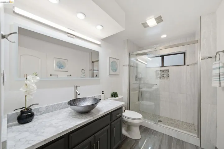 Bathroom featuring a glass-enclosed shower with mosaic tile accents, a floating vanity with a vessel sink, and a large mirror with integrated lighting