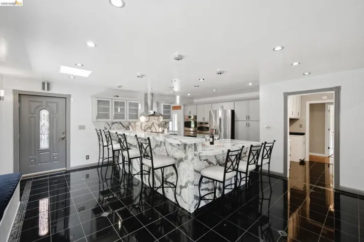 Spacious kitchen featuring a large waterfall-edge island, black tile flooring, recessed lighting, a skylight, and stainless steel appliances