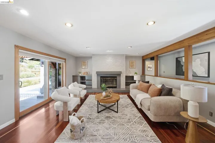 Spacious living area featuring rich wood-finish flooring, a fireplace with a stone hearth and textured tile surround, and recessed lighting