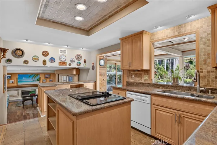 Beautiful wood cabinetry kitchen with granite countertops and mosaic backsplash, island with cooktop, stainless steel sinks, stainless steel ovens.