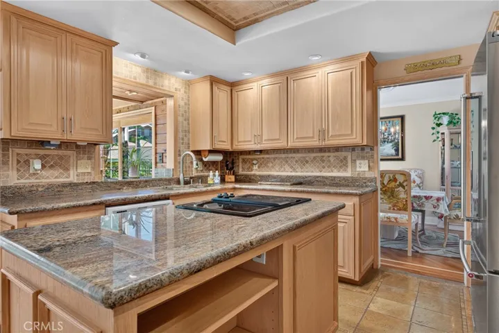 Beautiful wood cabinetry kitchen with granite countertops and mosaic backsplash, island with cooktop, stainless steel sinks, stainless steel ovens.