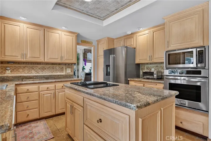 Beautiful wood cabinetry kitchen with granite countertops and mosaic backsplash, island with cooktop, stainless steel sinks, stainless steel ovens.