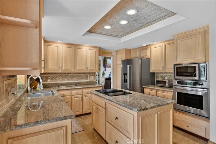 Beautiful wood cabinetry kitchen with granite countertops and mosaic backsplash, island with cooktop, stainless steel sinks, stainless steel ovens.