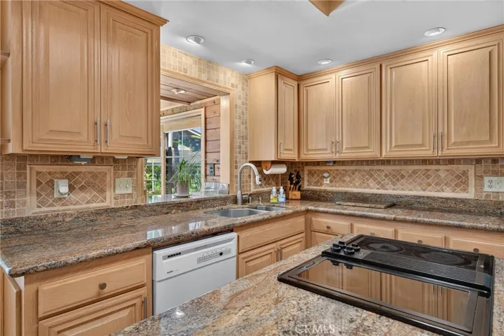 Beautiful wood cabinetry kitchen with granite countertops and mosaic backsplash, island with cooktop, stainless steel sinks, stainless steel ovens.
