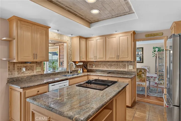 Beautiful wood cabinetry kitchen with granite countertops and mosaic backsplash, island with cooktop, stainless steel sinks, stainless steel ovens.