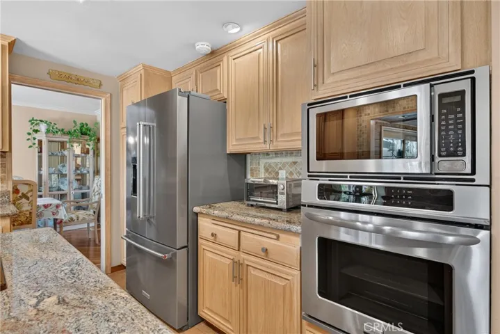 Beautiful wood cabinetry kitchen with granite countertops and mosaic backsplash, island with cooktop, stainless steel sinks, stainless steel ovens.