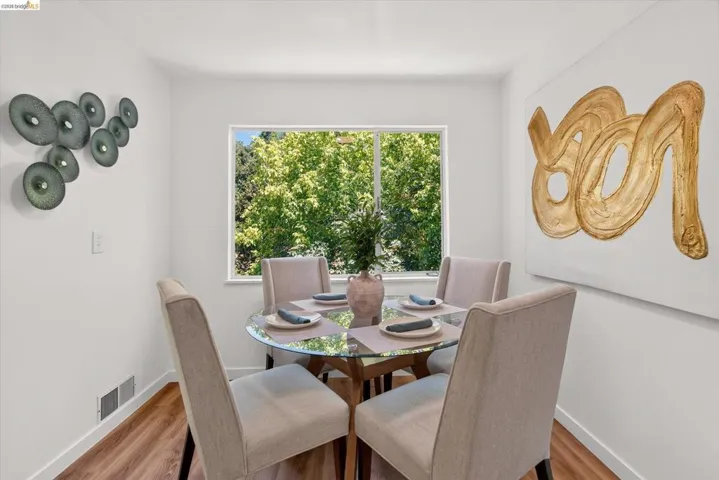 Bright dining area featuring a large window, wood-finish flooring, and crisp white walls