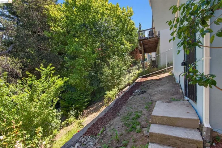 Tiered concrete steps leading to a side yard with a sloped landscape and mature trees