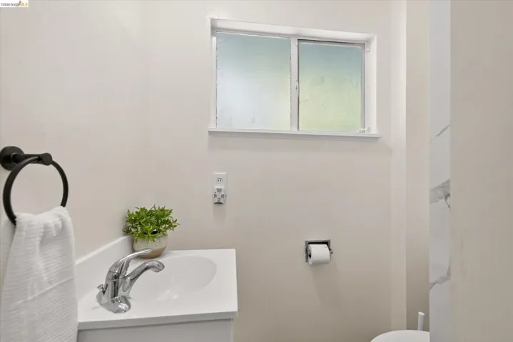 Bathroom featuring a single-pane window, white vanity with integrated sink, chrome faucet, and matte black towel ring