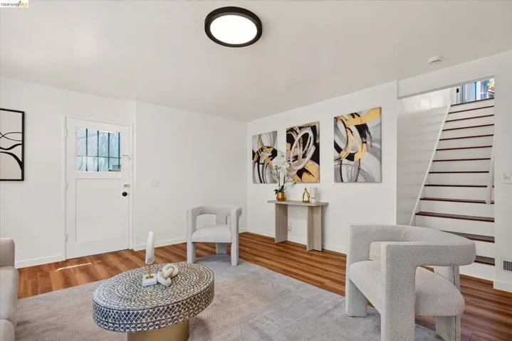 Bright living area featuring wood-finish flooring, a contemporary flush-mount ceiling light, and a staircase with white risers and dark treads