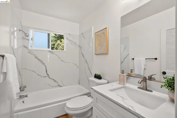 Bathroom featuring a vanity with an integrated sink, brushed nickel faucet, large wall mirror, and a white bathtub with marble-look wall surrounds