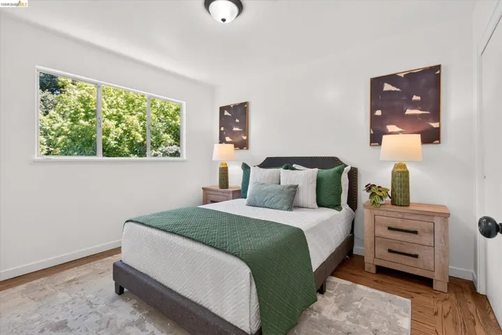 Bedroom featuring wood-finish flooring, a three-panel window, white walls, and a ceiling-mounted light fixture